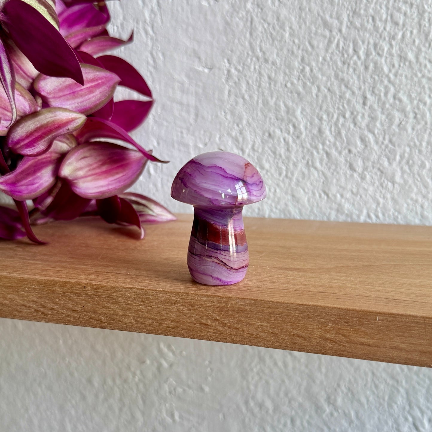 Purple calcite mushroom on a wooden shelf with pink flowers in the background