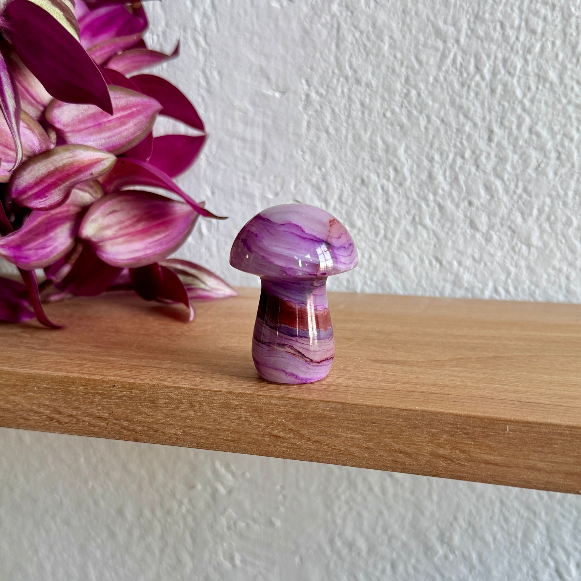 Purple calcite mushroom on a wooden shelf with pink flowers in the background