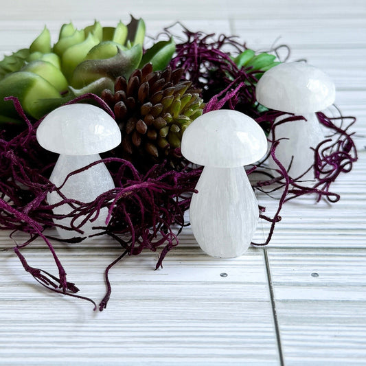 White selenite mushroom carvings on a surface with green and purple decorative elements.