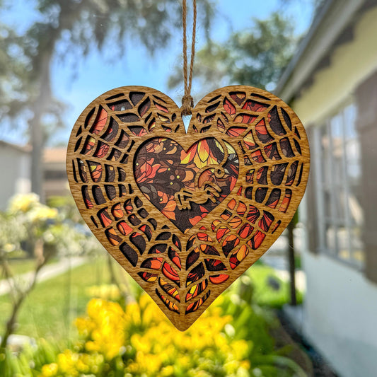 Spiderweb heart shaped suncatcher made from wood and acrylic hanging in window.
