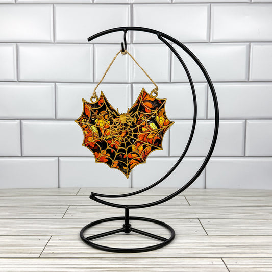 Spiderweb suncatcher made from wood and acrylic hanging on a metal stand in front of a white tiled wall.