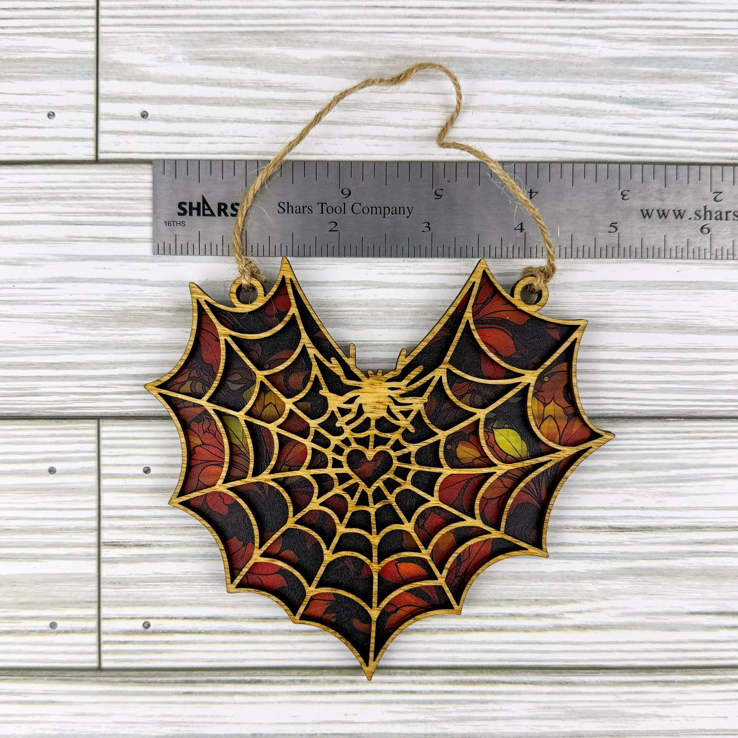 Maple leaf suncatcher made from wood and acrylic lying flat with a ruler showing the approximate width.