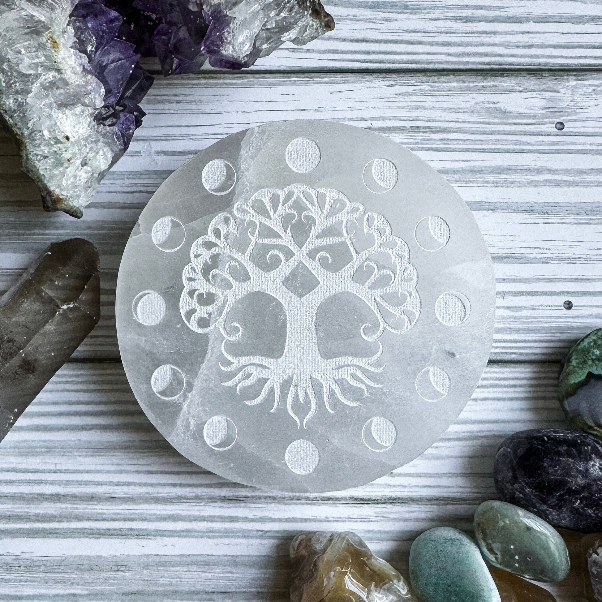 Selenite stone with tree of life design on a wooden surface with crystals around