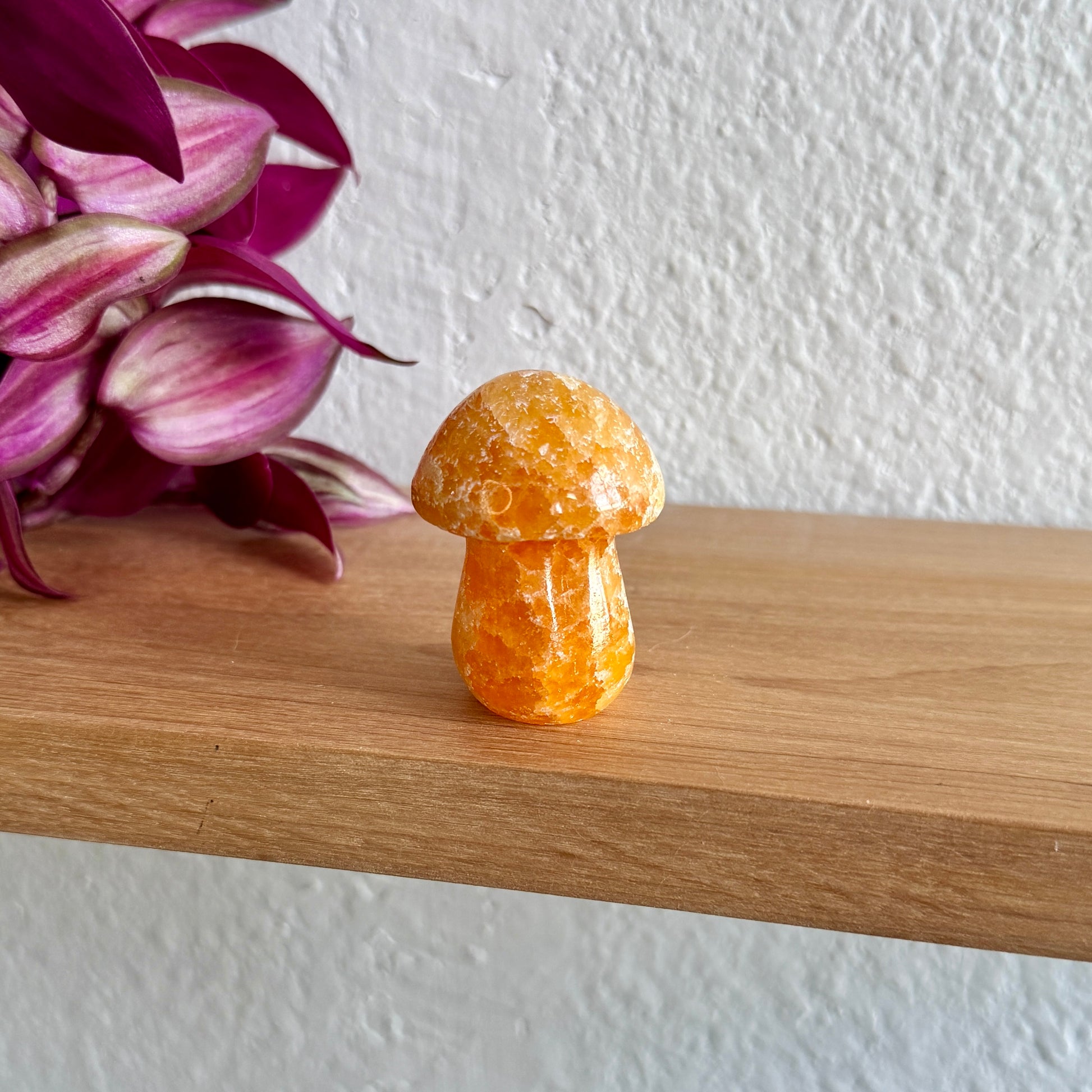 Yellow calcite crystal mushroom on a wooden surface with pink flowers in the background