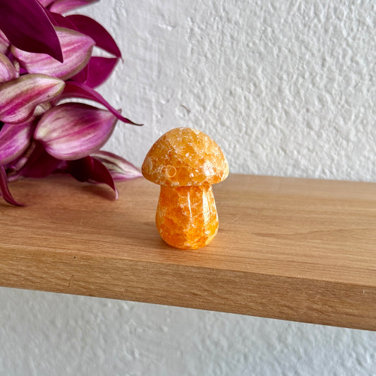 Yellow calcite crystal mushroom on a wooden surface with pink flowers in the background
